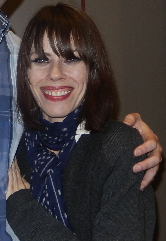 Close-up portrait of Fairuza Balk smiling, wearing a dark sweater and blue patterned scarf