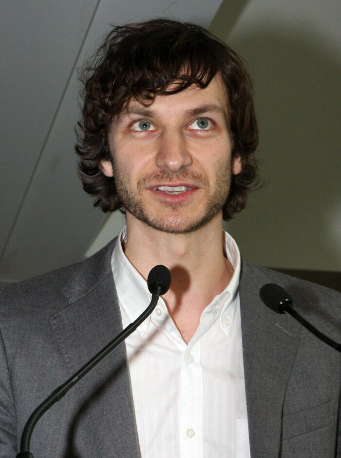 Gotye speaking at a podium during a public event with microphones