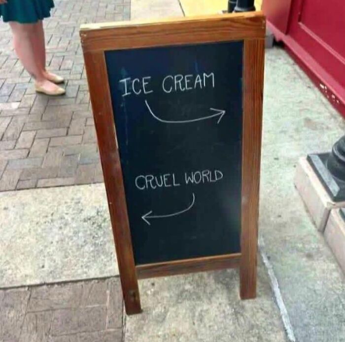Chalkboard sign humorously pointing ice cream right and cruel world left