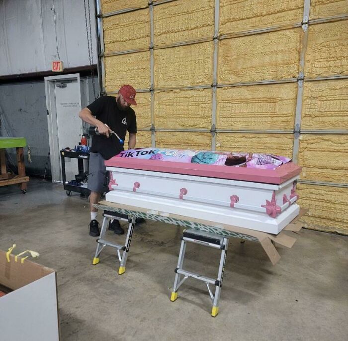 Man decorating a pink and white coffin in a workshop