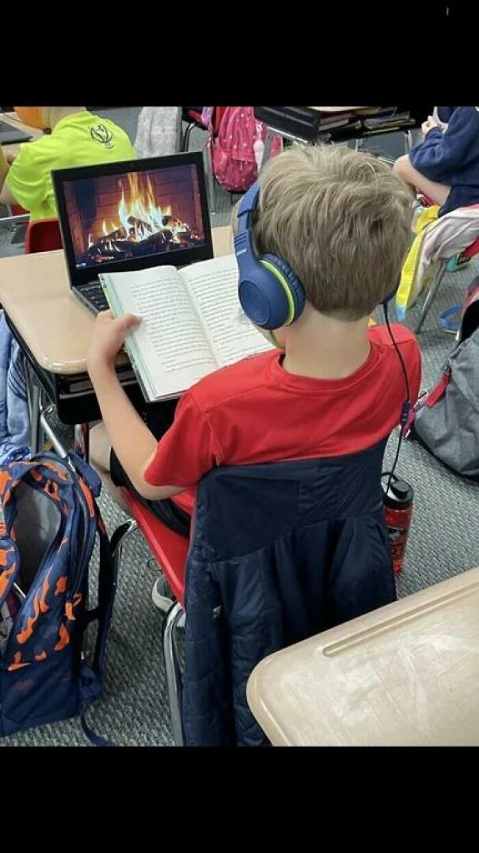 Young student reads book with laptop showing cozy fireplace