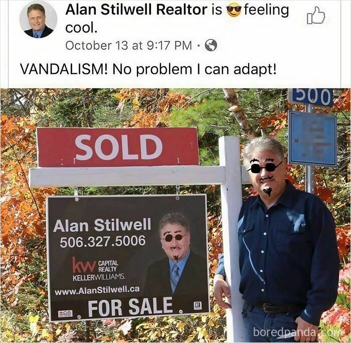 Realtor smiling beside vandalized real estate sign with drawn-on glasses and mustache