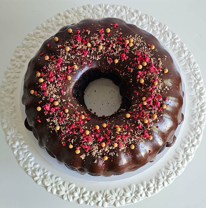 Chocolate bundt cake with glossy glaze and sprinkled toppings on white plate