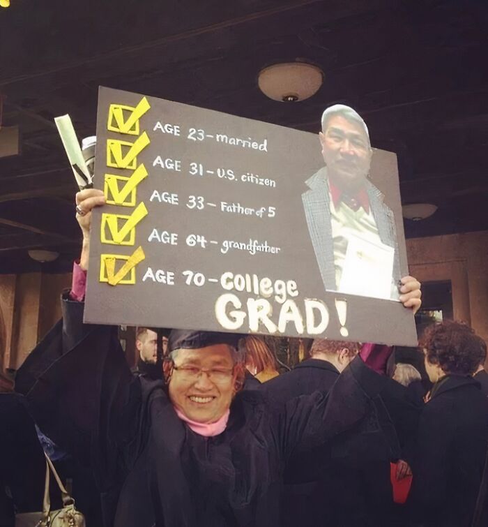 Graduate proudly holds sign showing life milestones including college graduation at 70