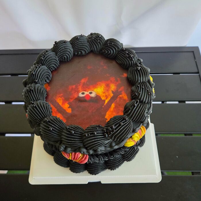 Round cake with black frosting and an image of fiery Elmo character on top