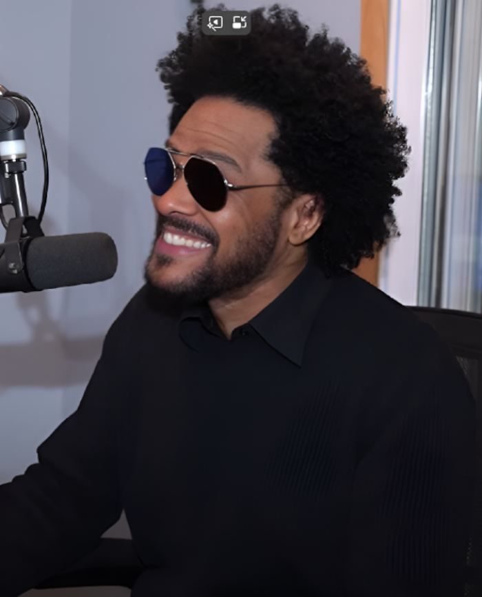 Maxwell smiling during a radio interview wearing sunglasses and black shirt