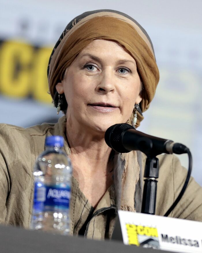 Melissa McBride speaking at a panel with microphone and water bottle in front