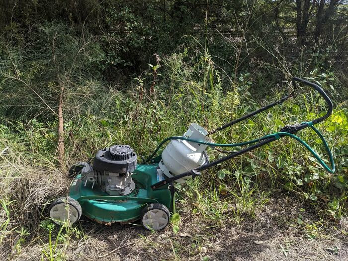 A green lawnmower with a propane tank attached, sitting in tall grass. A clever solution for powering the machine.