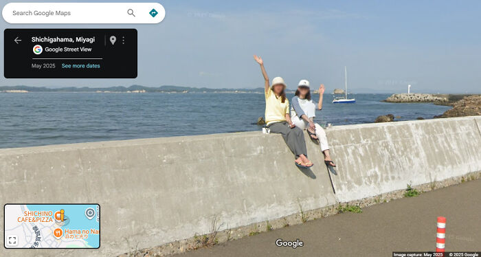 Two people waving sitting on sea wall captured in Google Maps Street View