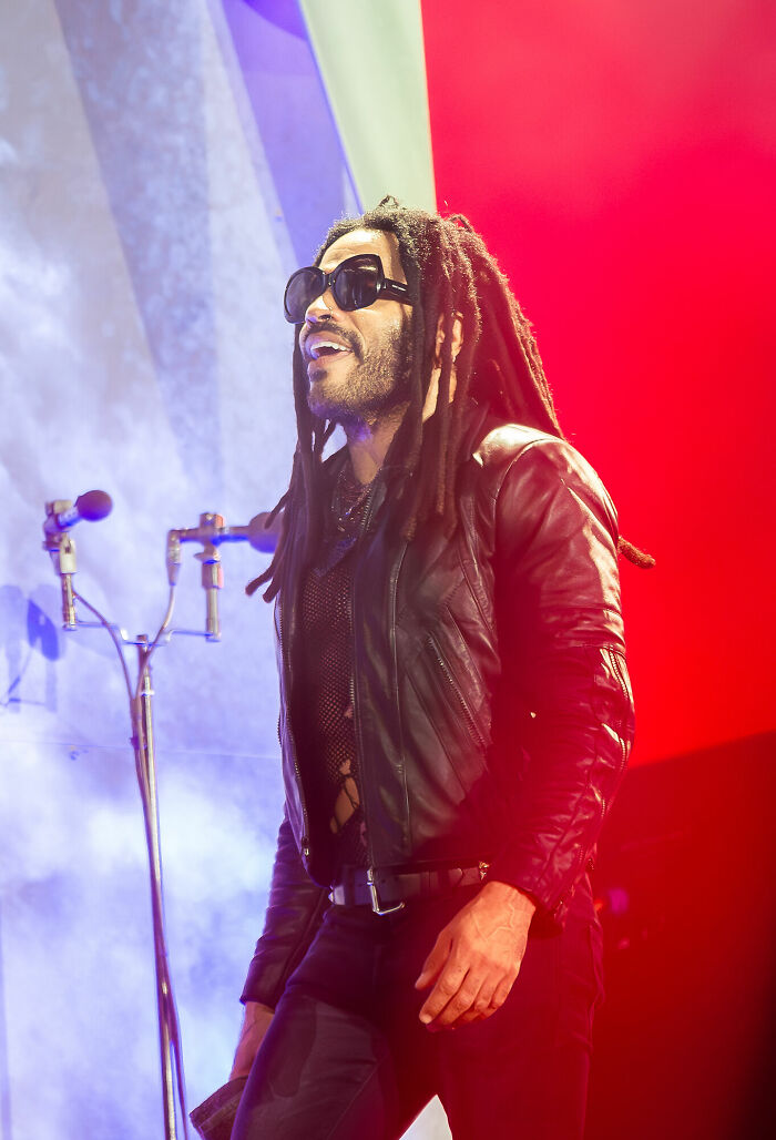 Lenny Kravitz performing on stage wearing sunglasses and a leather jacket amidst colorful lighting