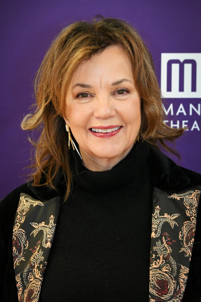 Portrait of Margaret Colin smiling at an event with a purple background and patterned jacket