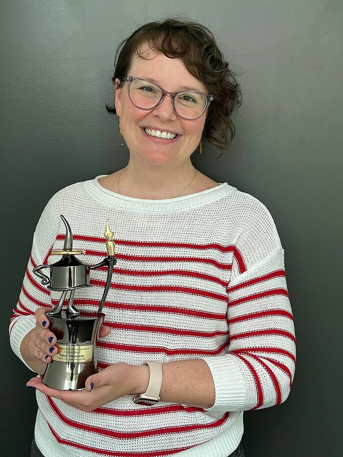 Raina Telgemeier smiling and holding an award trophy against a dark background