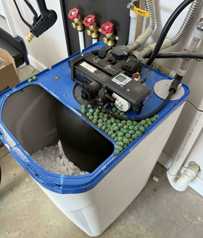 Open water softener with salt pellets spilled out near pipes
