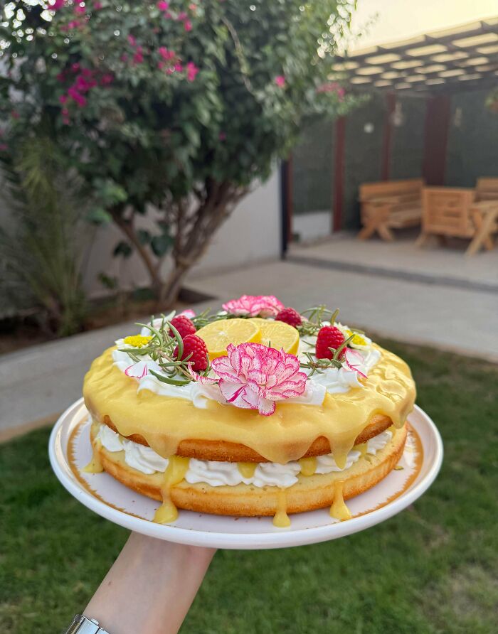 Delicious treats by bakers: A hand holds a beautiful lemon layer cake topped with flowers, a delightful dessert.