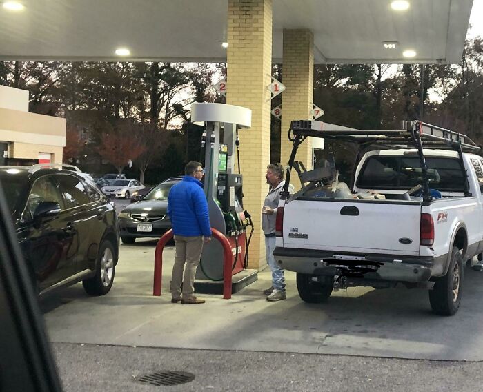 Two men at gas station discussing near a white pickup truck