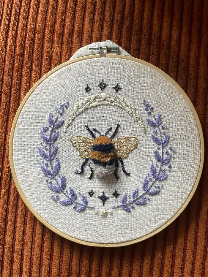 A detailed bee embroidery project with a crescent moon, lavender wreath, and stars in a wooden hoop