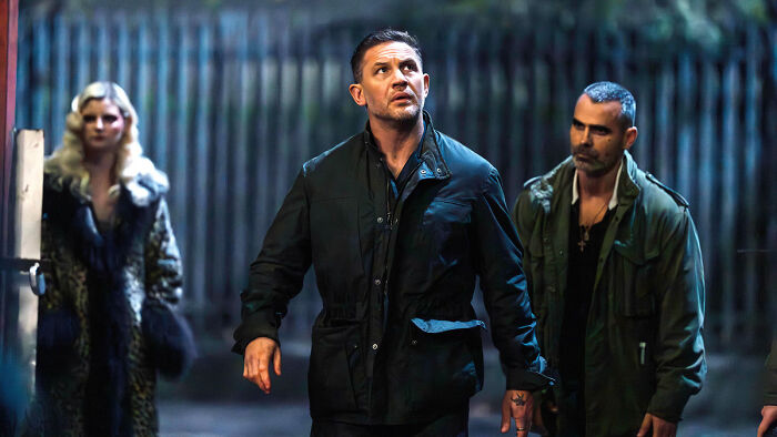 Tom Hardy in dark jacket on Mobland set with two co-stars during nighttime scene Tom Hardy in dark jacket on Mobland set with two co-stars during nighttime scene