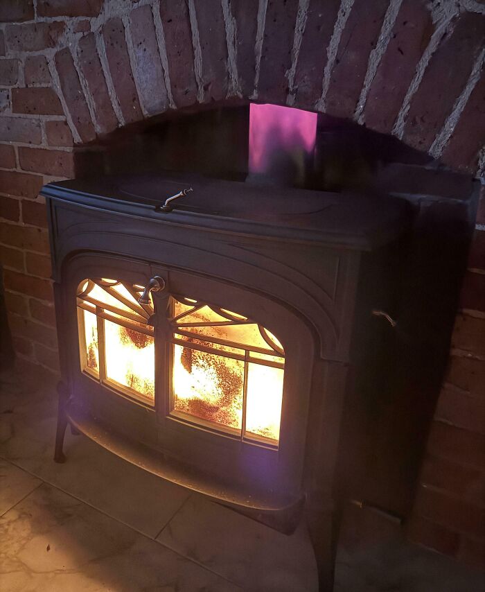 Wood-burning stove with fire inside against a brick wall