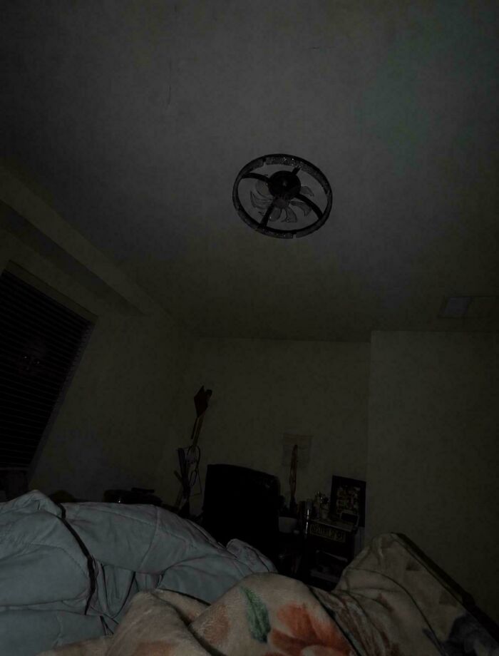 Ceiling fan casting shadows in dark bedroom with blankets in foreground