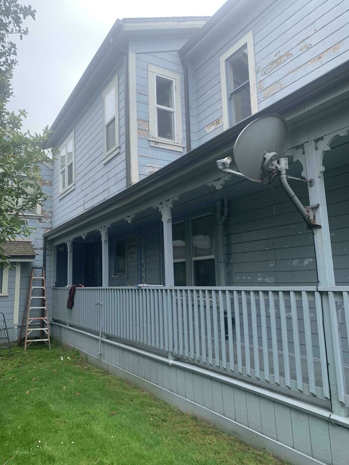 Blue weathered house with peeling paint and a satellite dish on balcony