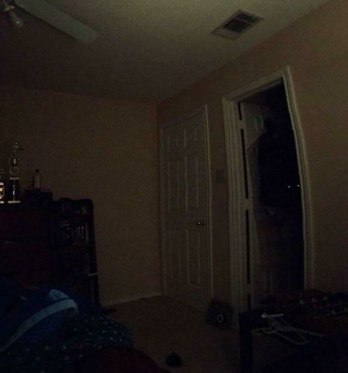 Dark room with faint lights revealing a mysterious figure at the door