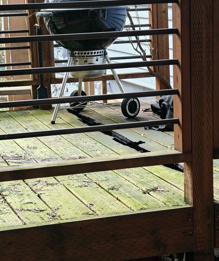 Worn wooden deck with large cracks beneath a charcoal grill