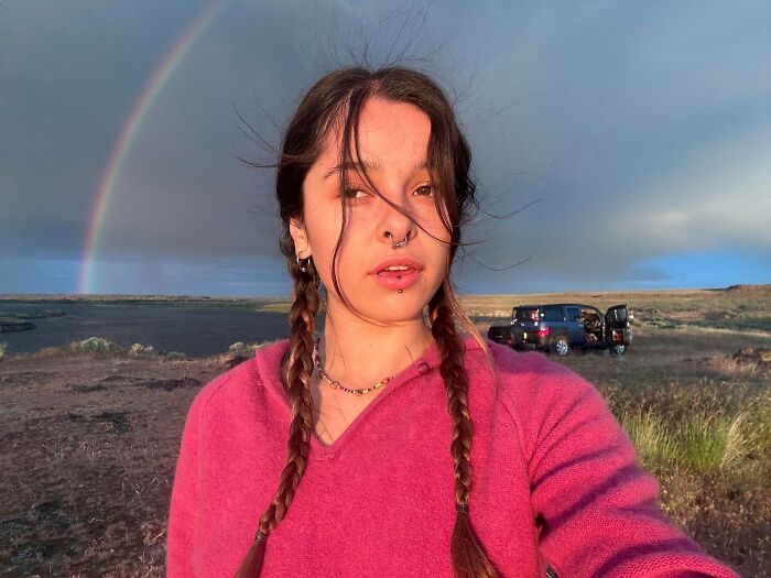 Woman with braids taking selfie outdoors with rainbow in background