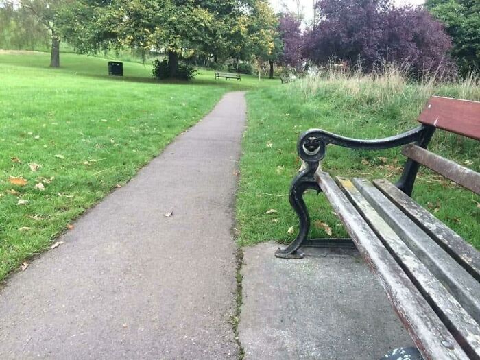 Park bench with armrest blending into the nearby path and grass detail