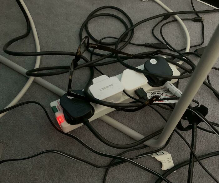 Tangled black charging cables plugged into power strip on carpet