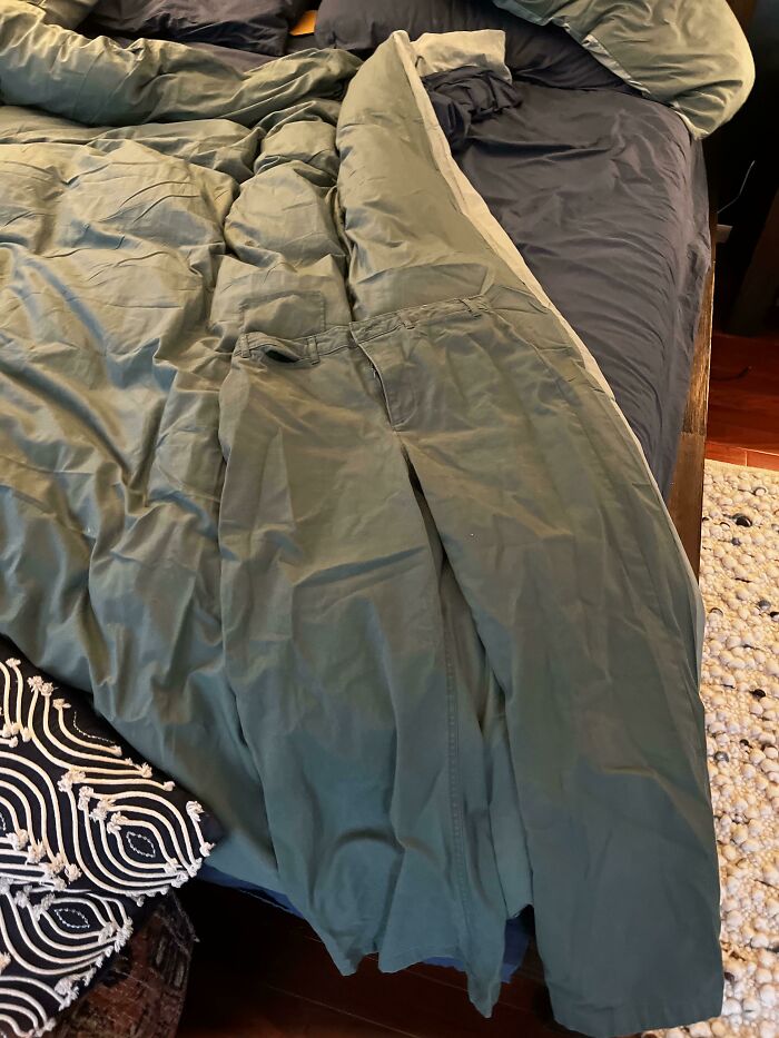 Green pants camouflaged inside matching green bedspread on messy bed