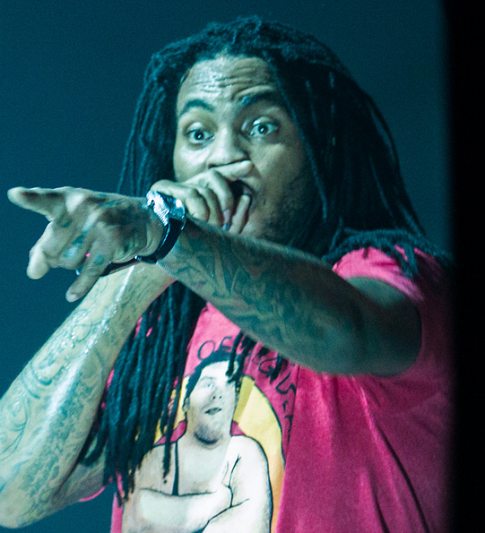 Waka Flocka Flame performing on stage with microphone in hand, wearing a red graphic t-shirt
