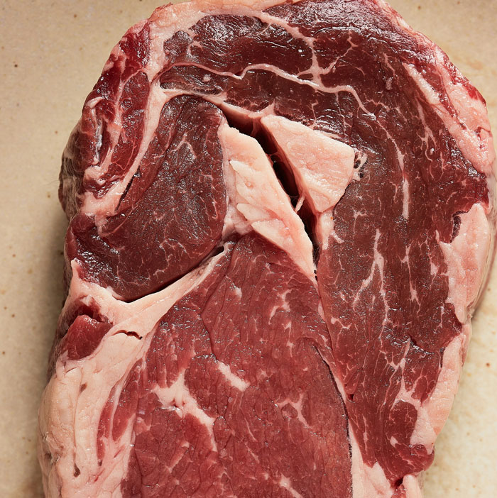 A close-up of a raw ribeye steak, showcasing the marbled red meat and white fat. One of the weirdest packages.