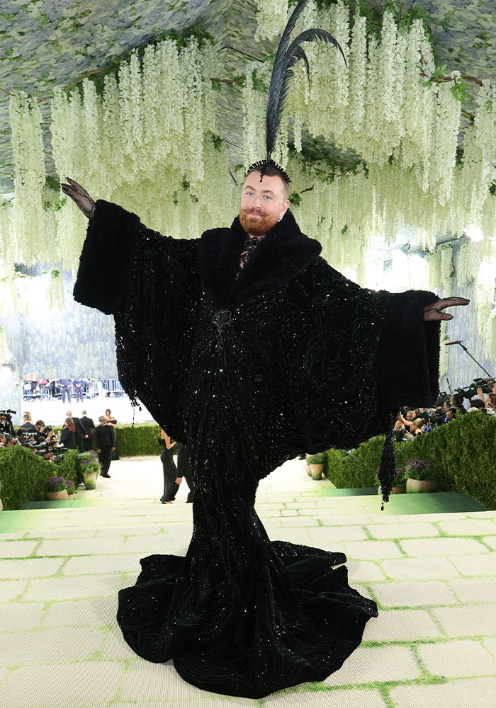 A person with a ginger beard in an extravagant black, sequined gown with a feather headpiece. Worst dressed stars at Met Gala 2026.
