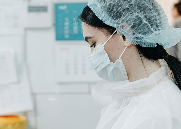 A young woman in medical scrubs, a face mask, and a hair net. She's a professional, unlike people of low intelligence.