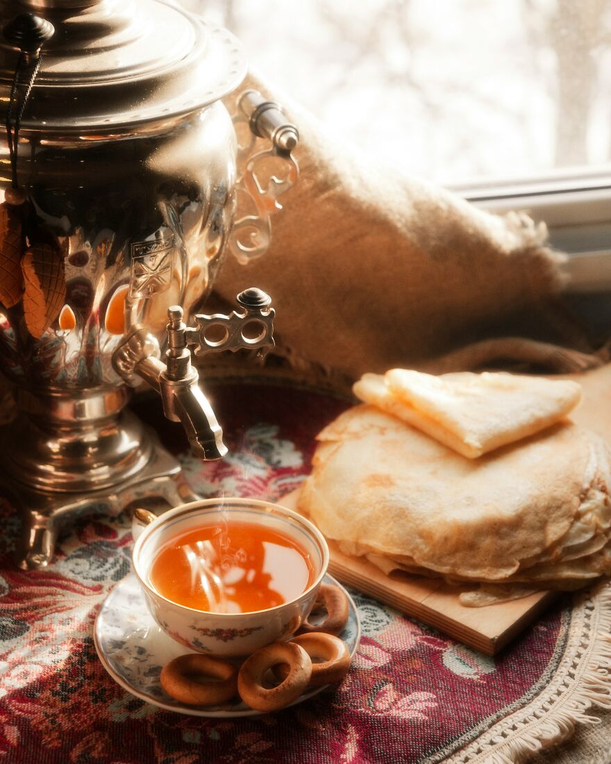 Warm tea poured from a samovar into a cup, with a stack of pancakes and pastries, highlighting traditional diets.