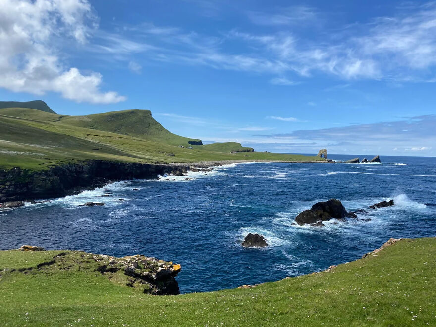 Dramatic coastline with lush green hills and a deep blue ocean, waves crashing. An isolated place on Earth.