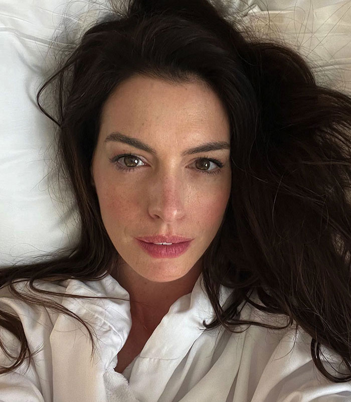 Anne Hathaway lying in a white robe, brown hair spread out, looking directly at the camera. Her acting is a highlight.