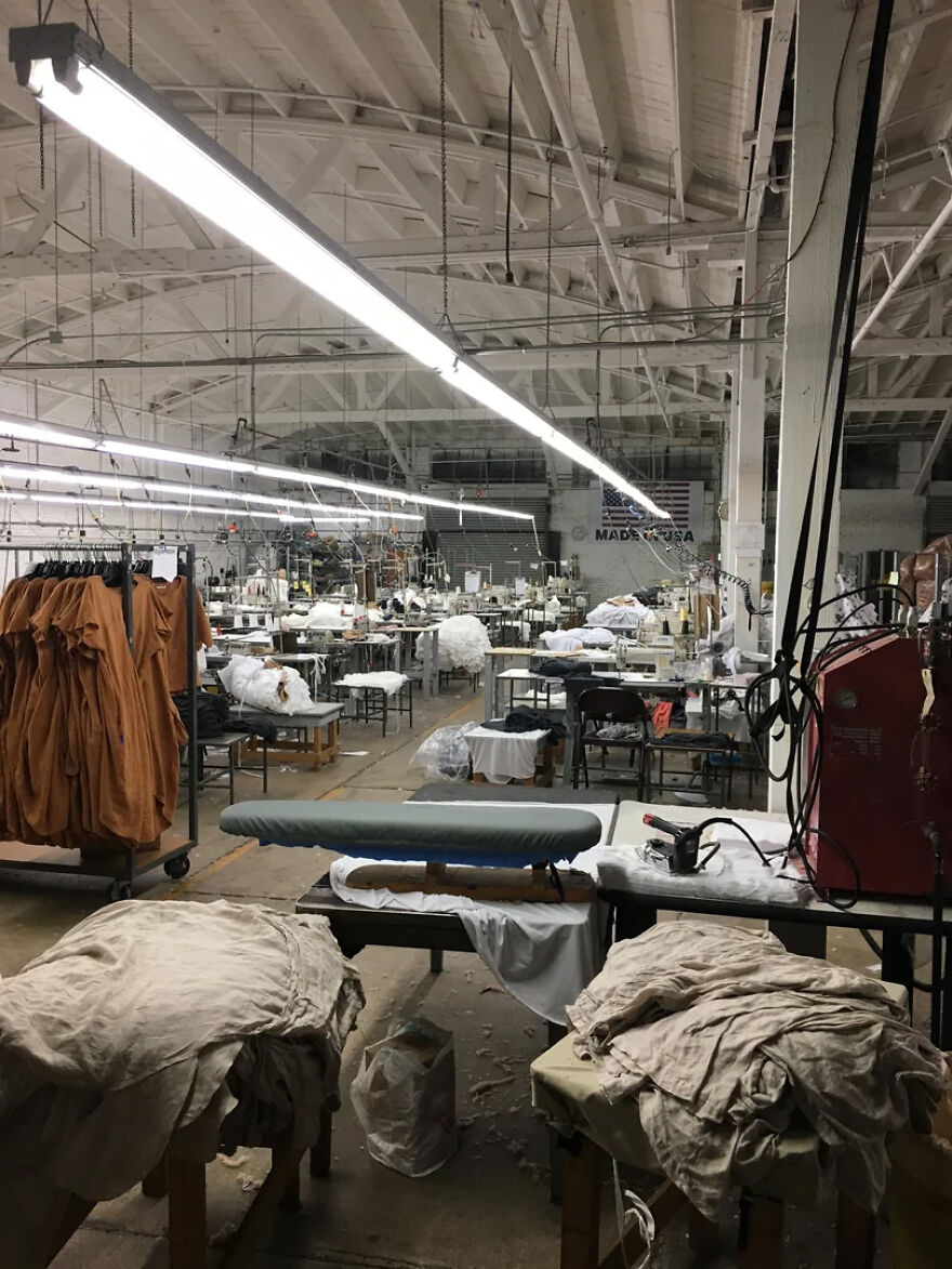 A busy, dimly lit garment factory with numerous sewing machines, clothing racks, and an ironing board, representing stressful jobs.