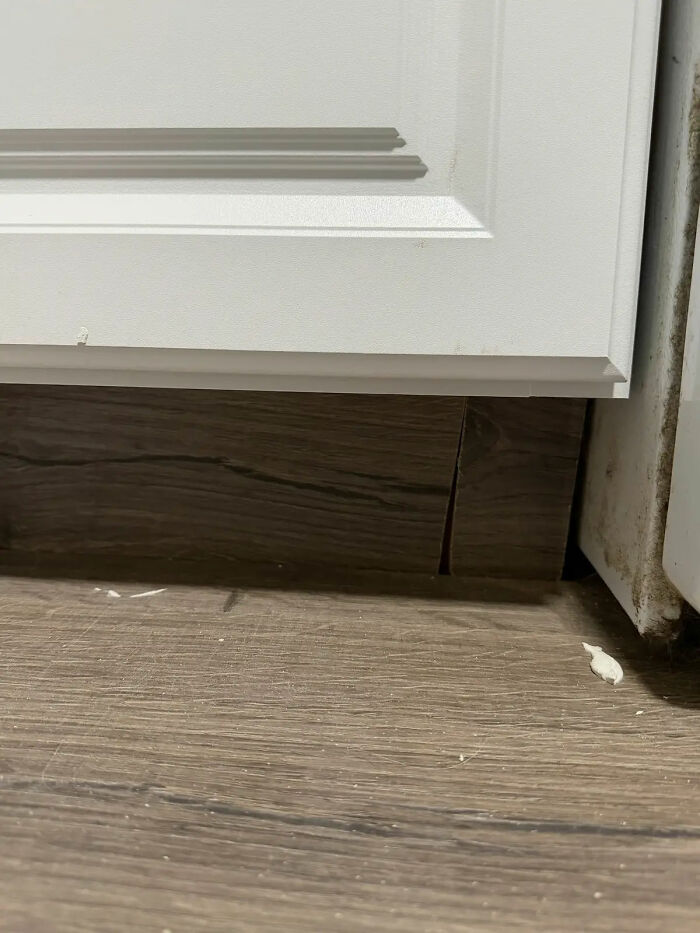 Poor contractor work: misaligned laminate flooring beneath a white cabinet, revealing a gap. A homeowner's horror story.
