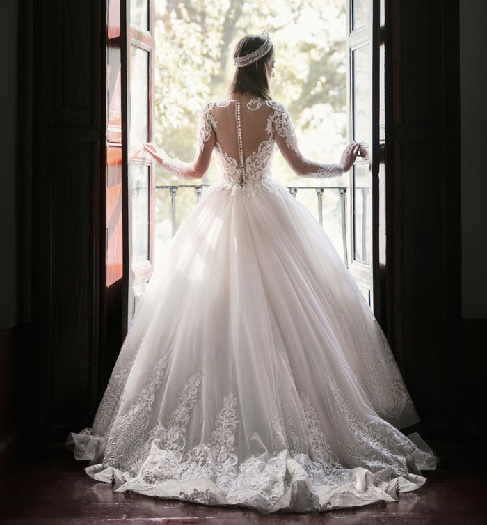 Bride in lace wedding gown standing by open balcony doors