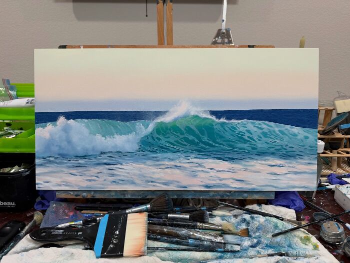 Painting of ocean waves on an easel with brushes and art supplies
