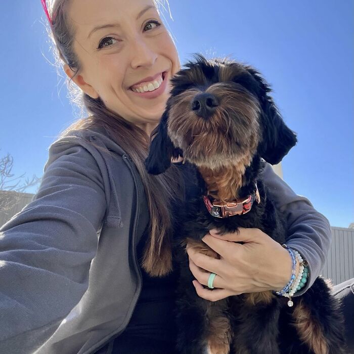 Smiling woman holding black dog outdoors on sunny day