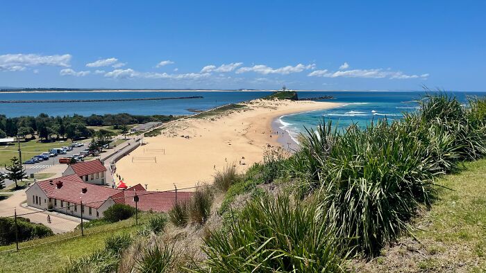 Sandy beach peninsula with grassy hill and ocean under blue sky geography fact
