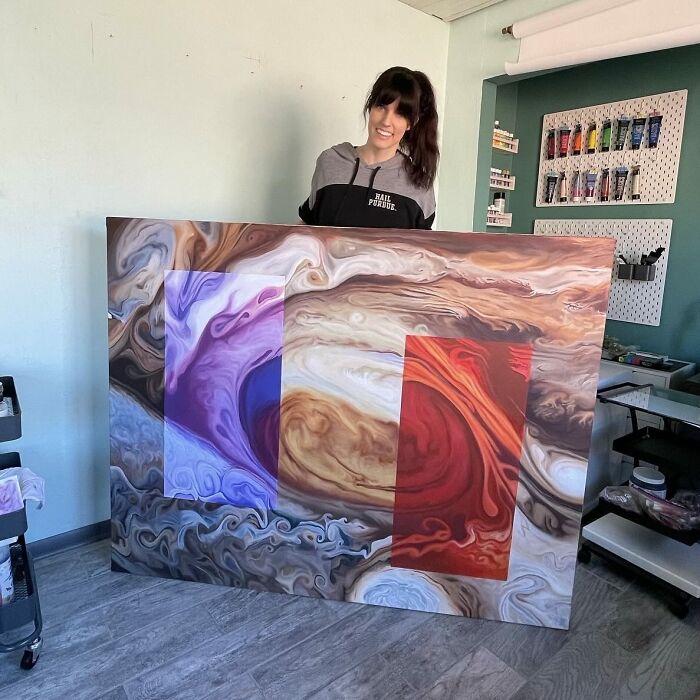 Woman artist holding large abstract painting in bright studio