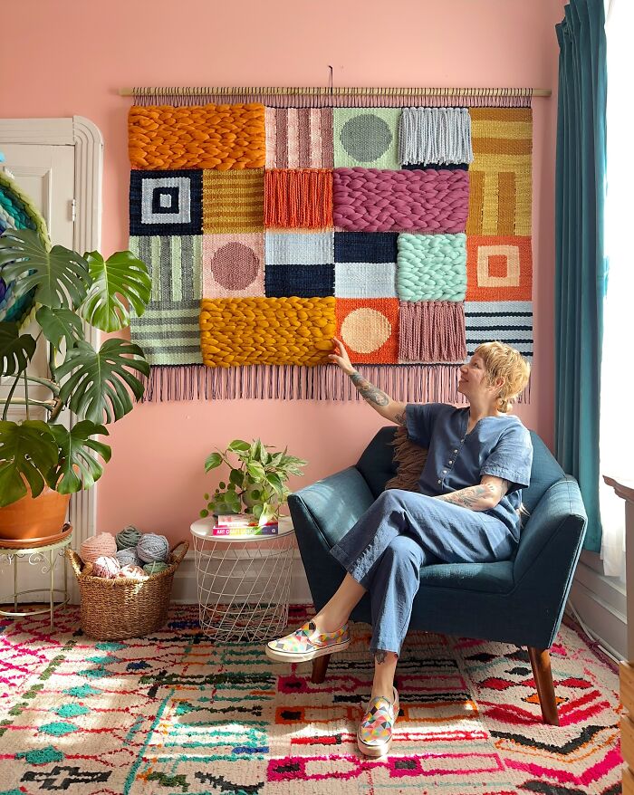 Woman sitting in a chair touching a colorful woven wall hanging in a stylish room