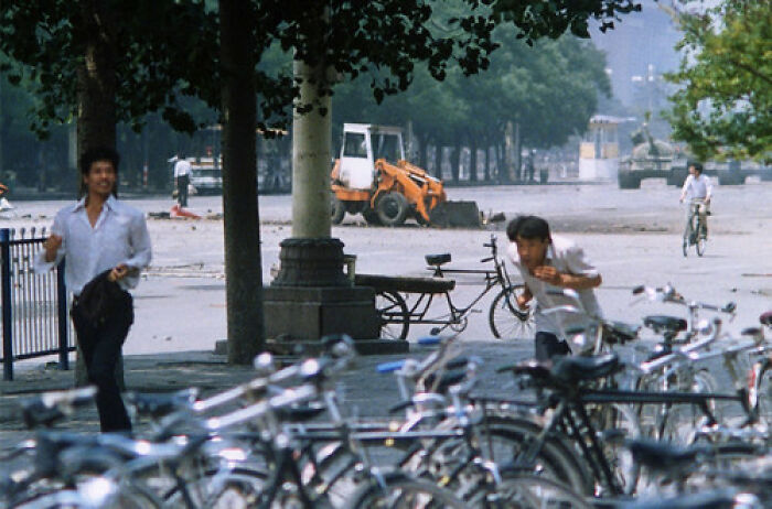 Creepy street scene with people and bicycles hiding behind trees with an excavator in the background