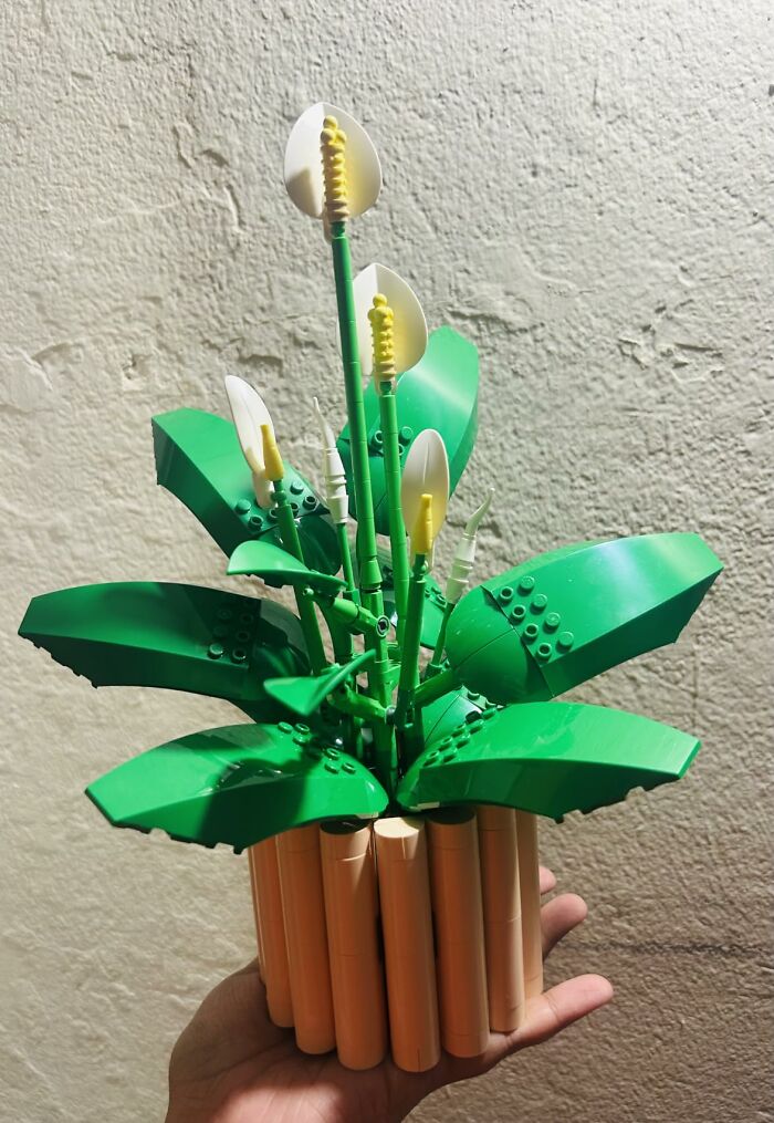 A hand holding a Lego plant with green leaves and white-yellow flowers, a unique last minute Mothers Day gift.