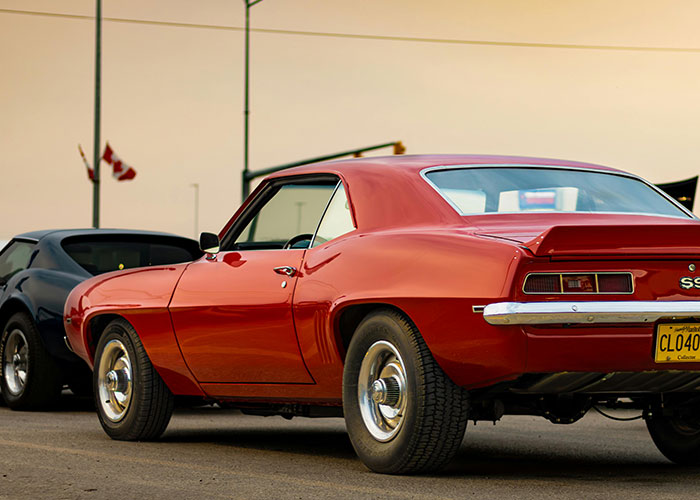 Red vintage muscle car with a black sports car in the background, challenging US stereotypes about cars.