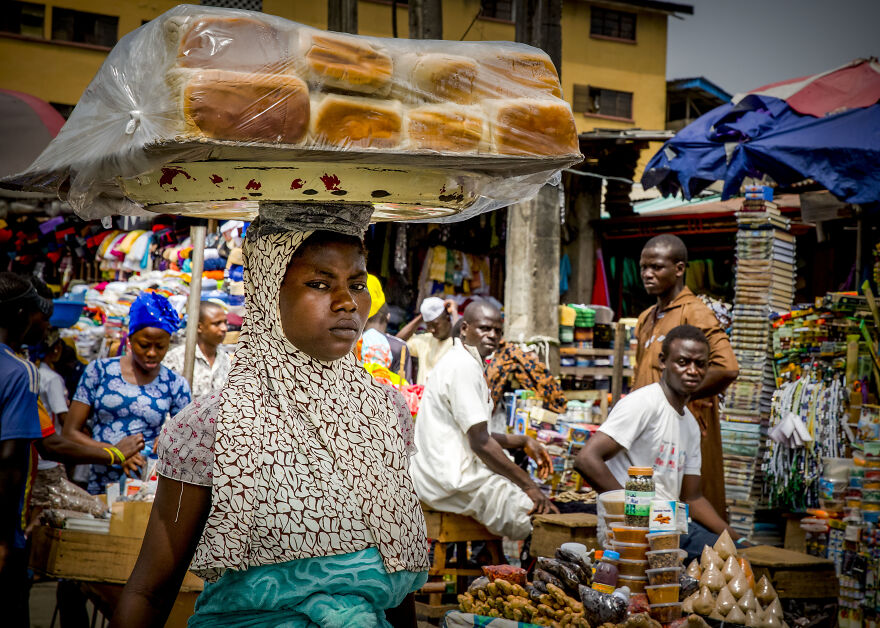 Woman balancing bread on her head in a busy market. This image relates to countries with the worst diets.