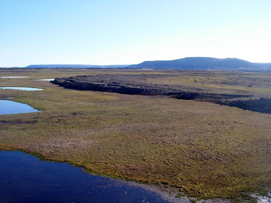 An aerial view of one of the most isolated places on Earth, showing a vast tundra landscape with small lakes and distant hills.